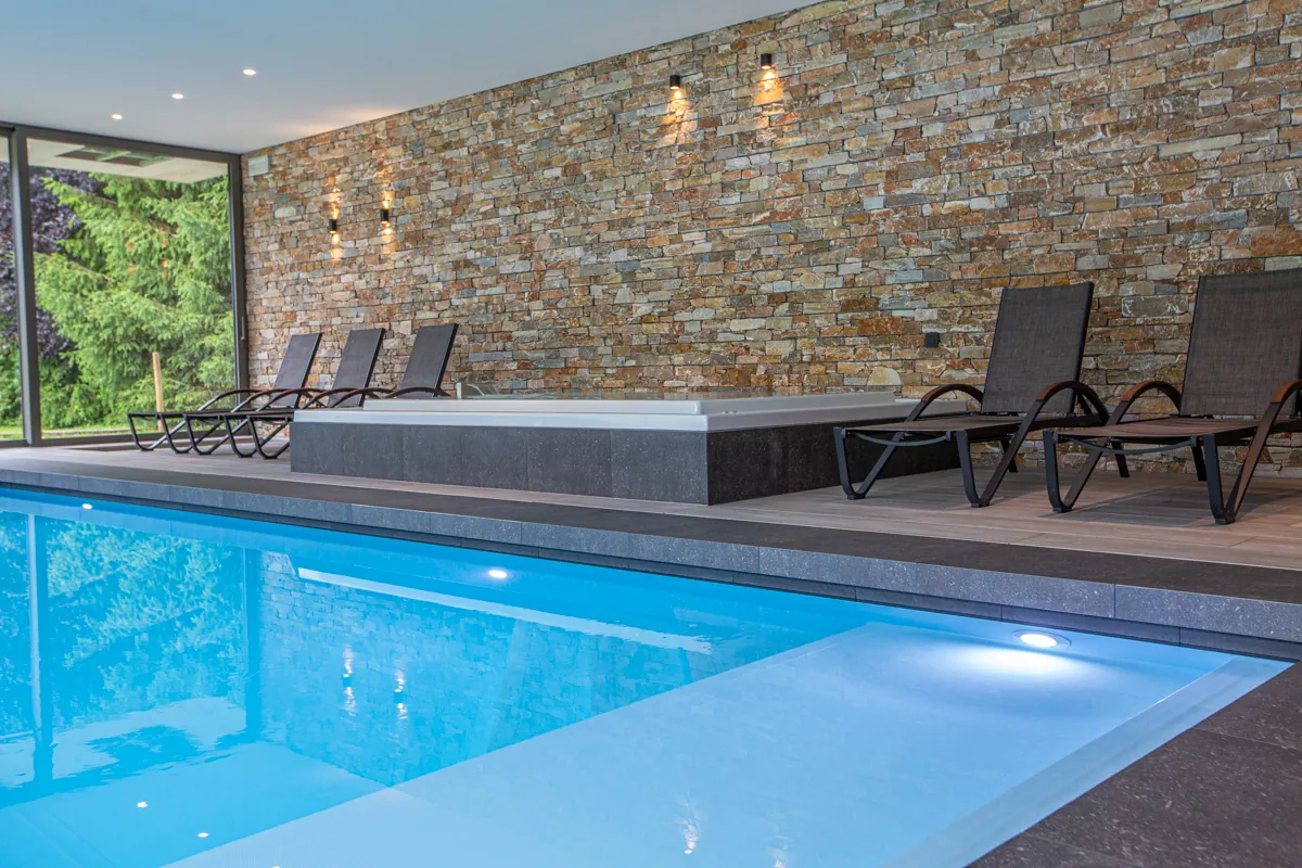 Piscine intérieure avec membrane armée RENOLIT ALKORPLAN 2000 Bleu clair, eau bleu piscine classique face à un mur en pierre