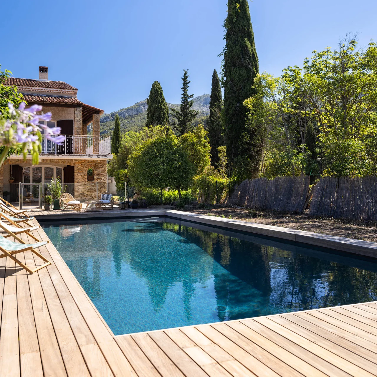 Piscine avec membrane armée BWT Be BRANE 3D Surface Black Reef, eau bleu nuit à l’effet miroir sur une terrasse en bois face aux collines