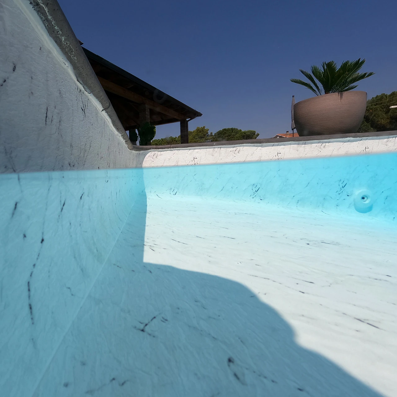 Vue au ras de l’eau d’une piscine avec membrane armée BWT Be BRANE 3D Surface Venatino Marble, effet marbre blanc veiné de gris sous un ciel bleu profond