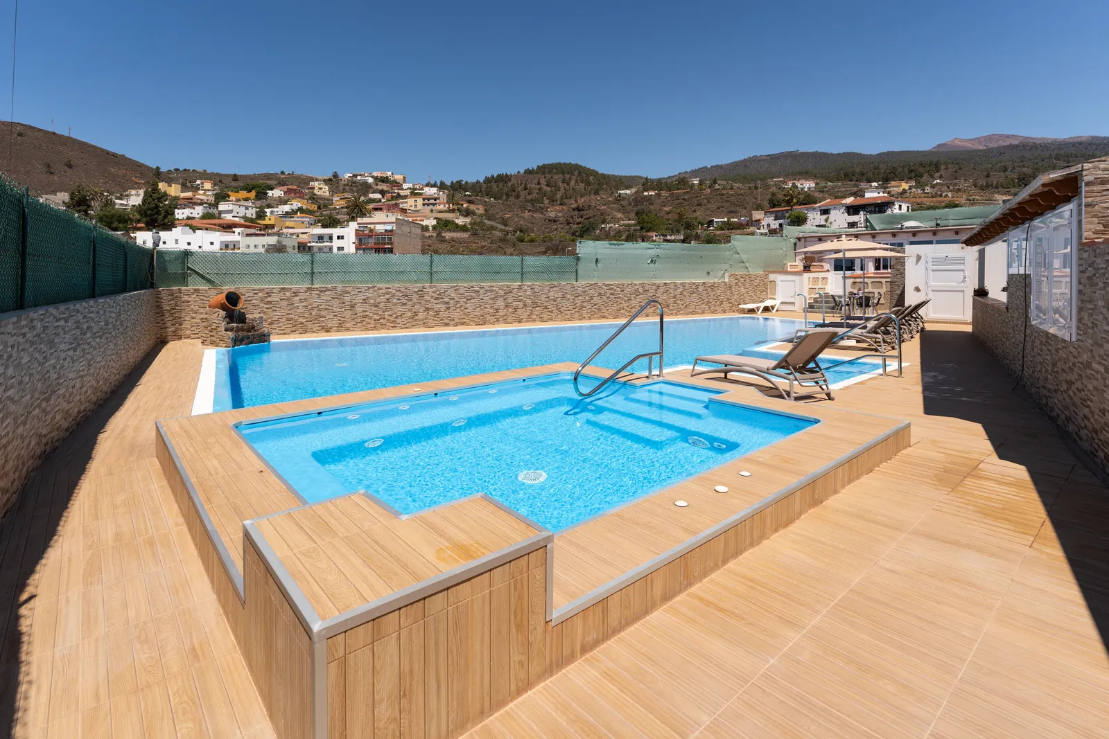 Piscine surélevée avec membrane armée RENOLIT ALKORPLAN Relief Bleu clair, terrasse en bois et vue sur les collines