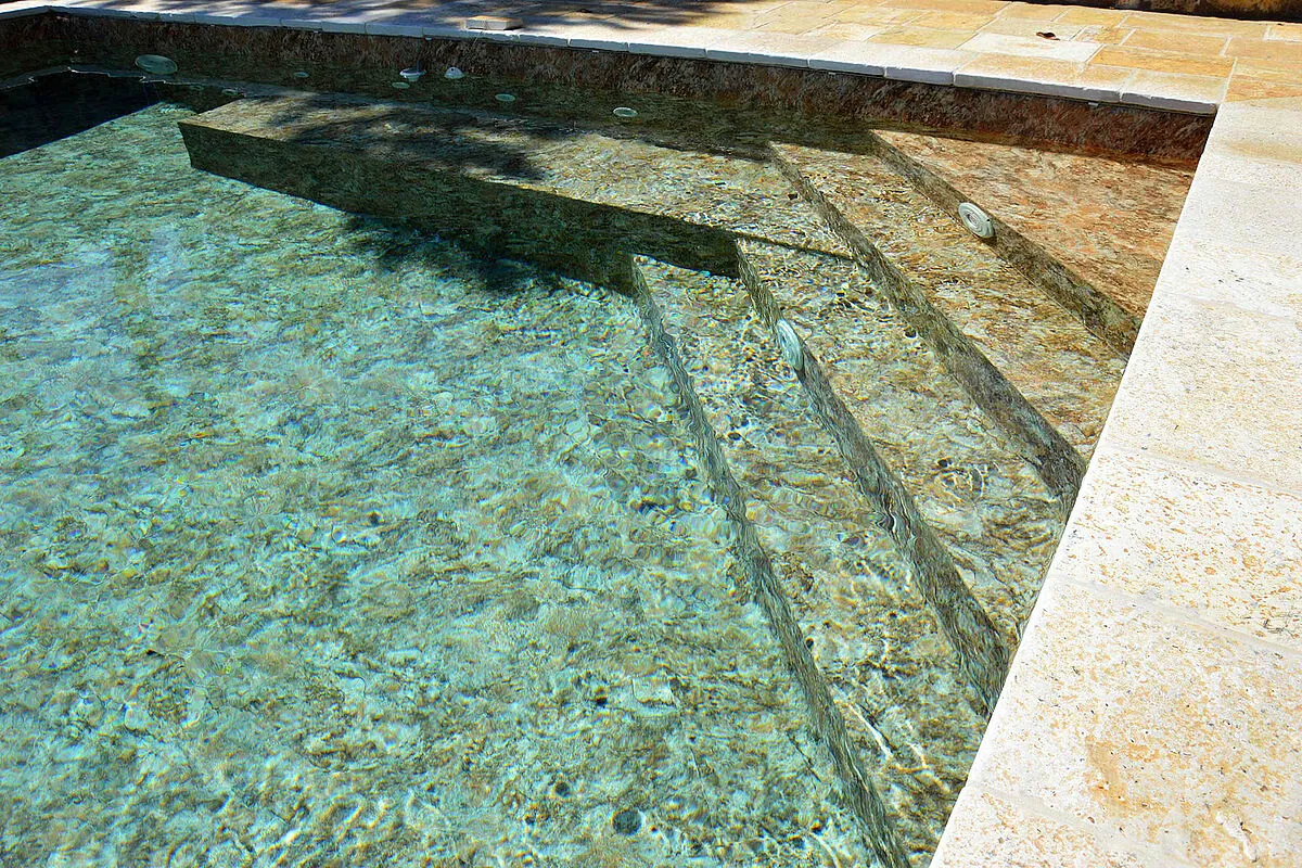 Marches de piscine avec membrane armée RENOLIT ALKORPLAN Touch Authentic, effet pierre brute aux tons rouille et eau cristalline