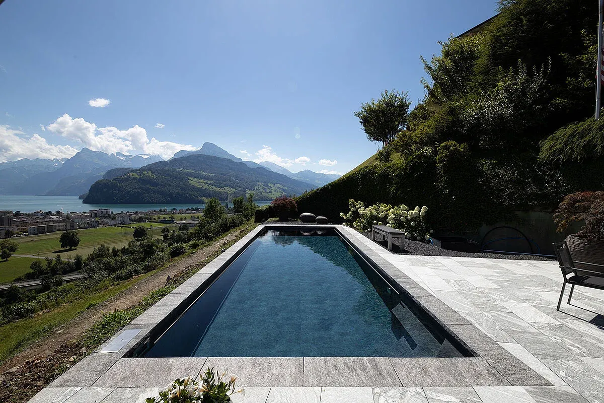 Piscine avec membrane armée RENOLIT ALKORPLAN Touch Elegance, effet ardoise sombre sur un terrain surplombant un lac et les montagnes