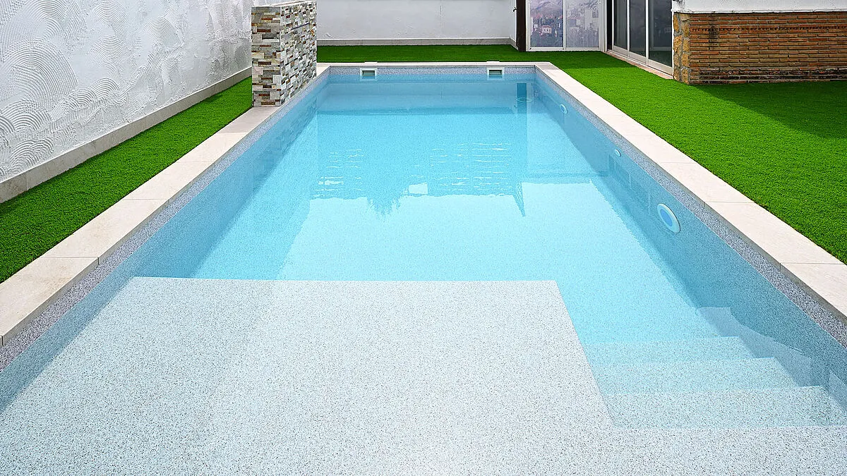 Piscine avec membrane armée RENOLIT ALKORPLAN Touch Origin, effet granit clair et eau turquoise dans un jardin avec gazon synthétique