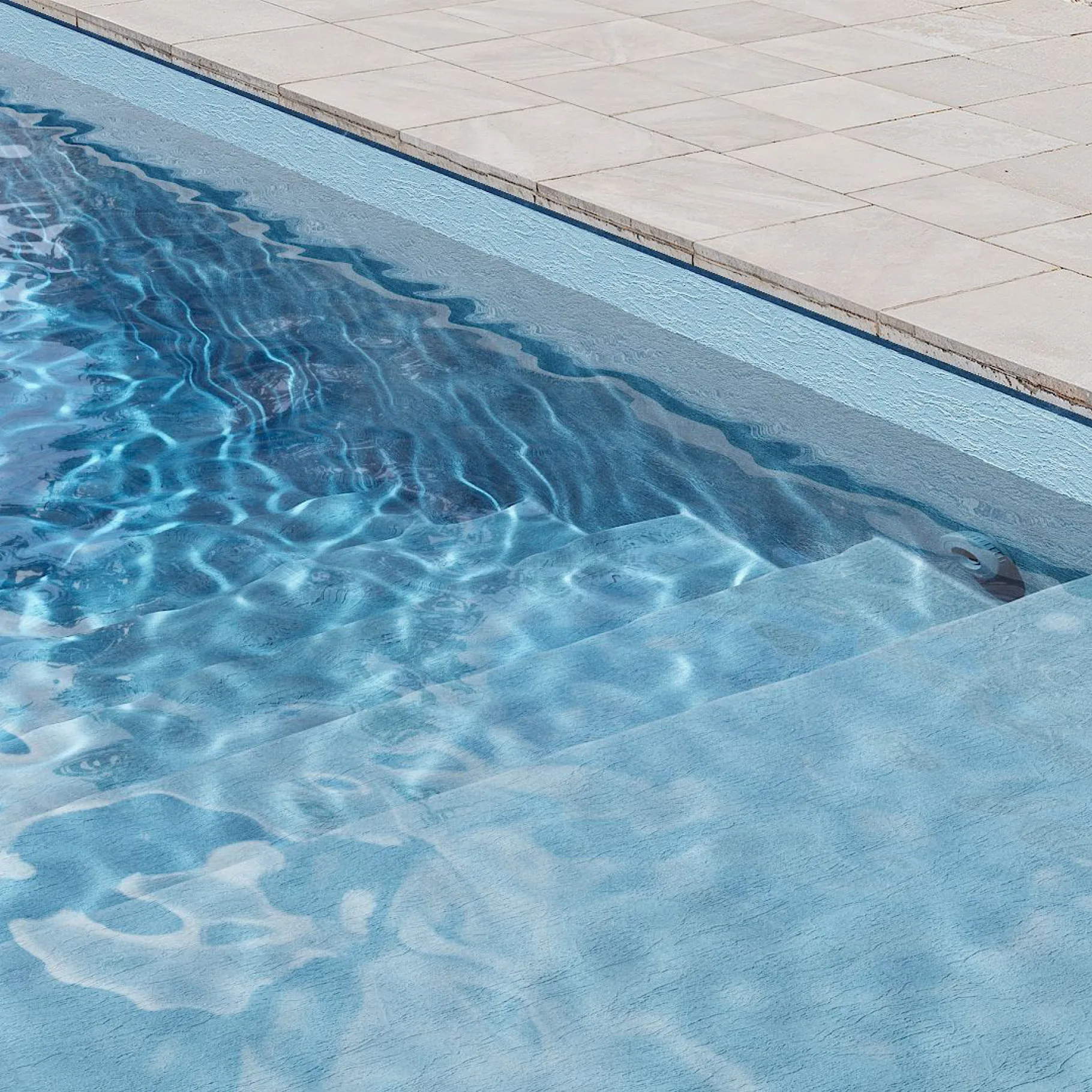 Marches de piscine avec membrane armée BWT Be BRANE Pureline Bleu clair, eau bleu clair et apaisante sur une terrasse en pierre claire